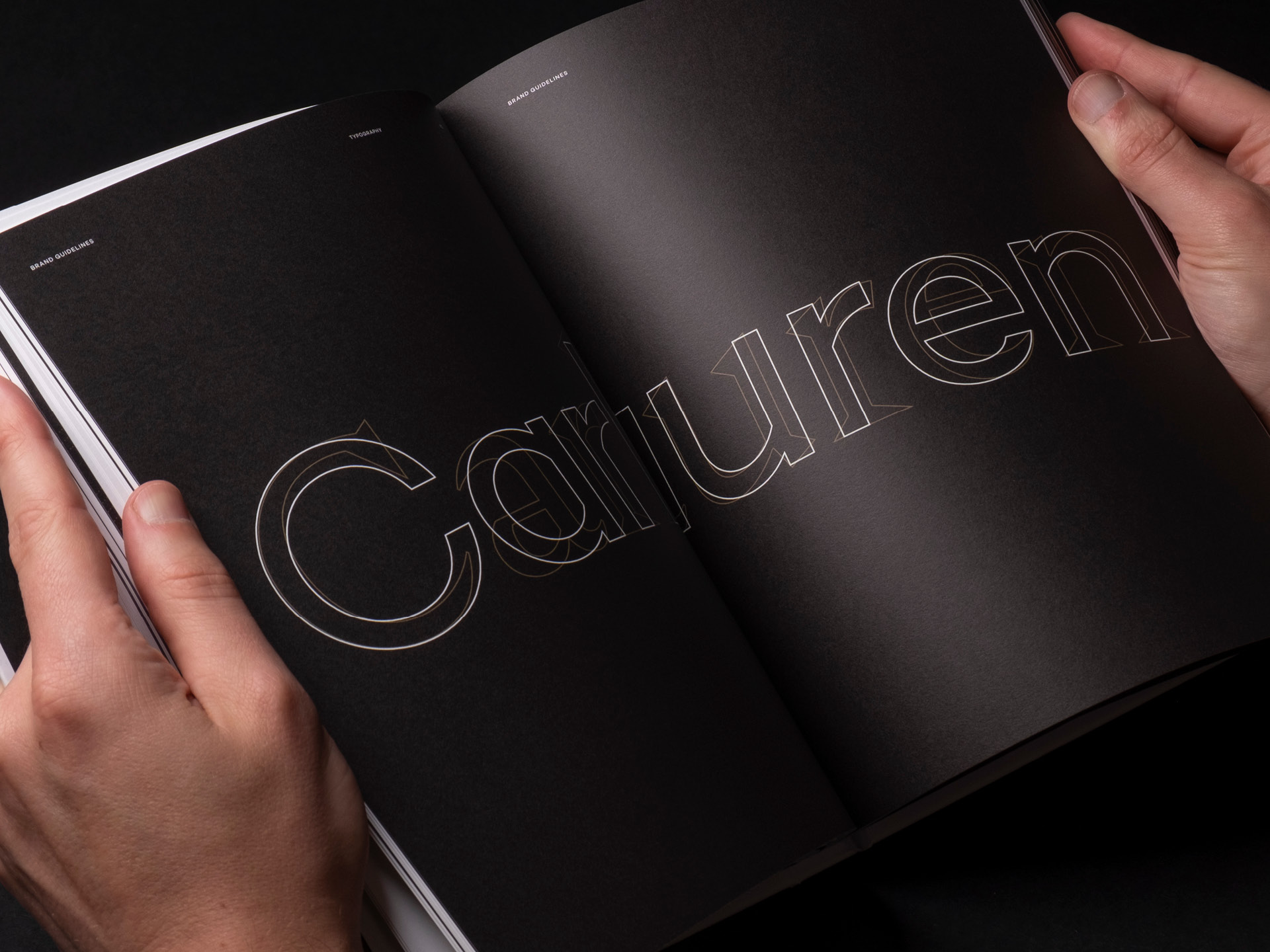 Two hands holding a printed spread from the Carlauren brand guidelines showcasing the two typefaces used in the brands communication