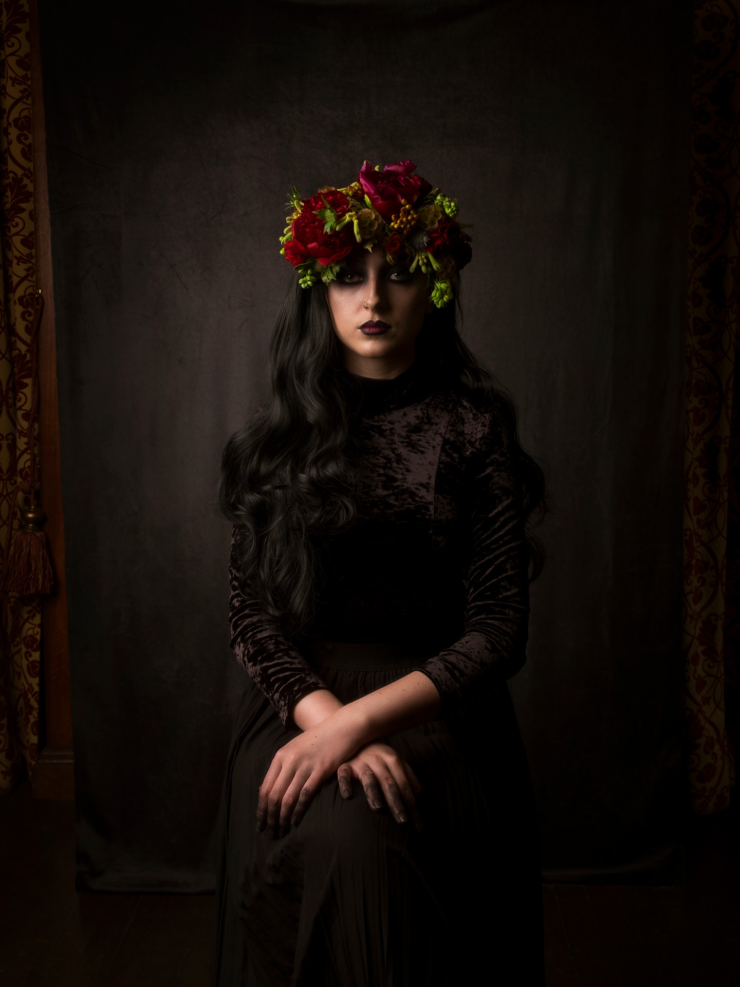 Sitting pose portrait photograph of model Bethan Perkins sat in classic renaissance style with black make-up applied to her eyes and hands in velour dress