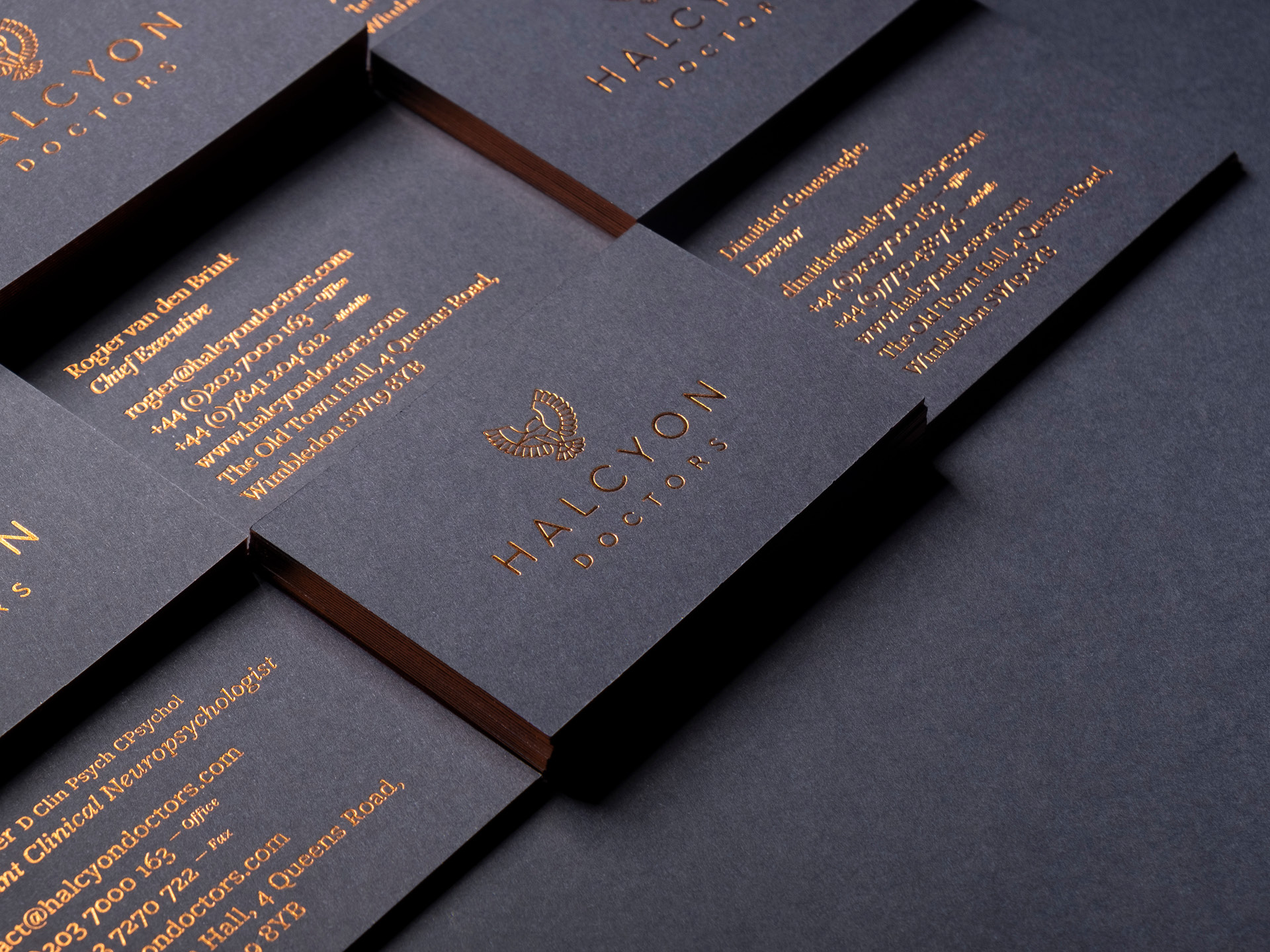 Various stacks of halcyon doctors business cards featuring the logo on one side and the contact details copper foiled on the other